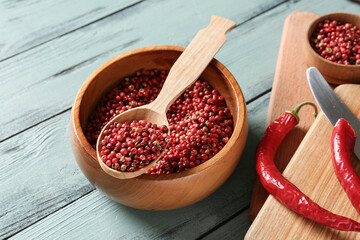 Bowl and spoon with red peppercorns on color wooden background