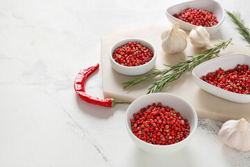 Bowls with red peppercorns and garlic on light background