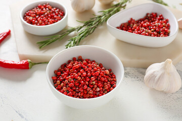 Bowls with red peppercorns and garlic on light background