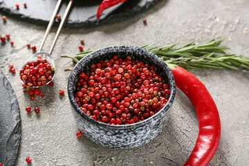 Bowl with red peppercorns on grey background