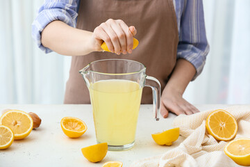 Woman squeezing lemon into jug at table in kitchen, closeup