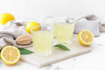 Fresh lemons and glasses of juice on light background