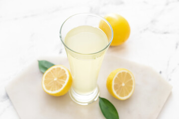 Fresh lemons and glass of juice on light background