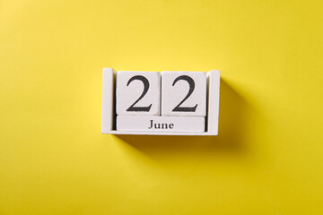 Wooden calendar on yellow background, top view, date 22 June