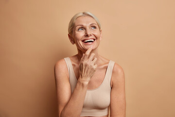Portrait of cheerful middle aged European woman smiles broadly concentrated above has perfect well...