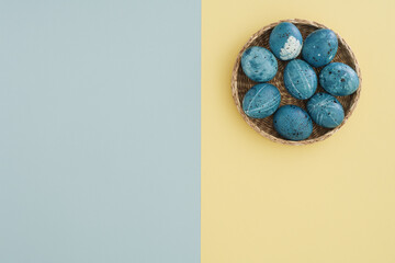 Easter concept on a two-tone yellow-blue background with a basket of Easter stylishly painted eggs. Copy space, top view, flat lay