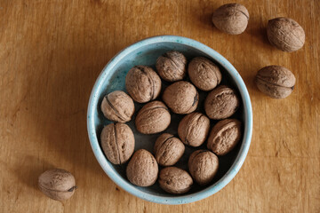 Walnuts in a blue ceramic bowl. Nuts are scattered on a wooden surface. Top view. 
