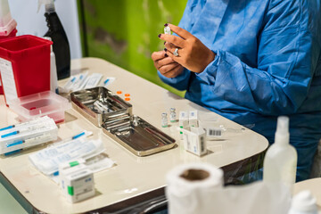 Coronavirus vaccine concept. Work team in light blue safety uniform, mask and glasses prepare the vial and syringe of the coronavirus vaccine. COVID-19 virus solution, cure for global pandemic.