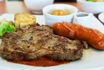 T-bone steak served with crisp sausage, Mashed potatoes, and Garlic bread accompanied by tomato sauce.