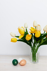 a bouquet of yellow tulips in a vase and in the church tradition Easter colorful eggs