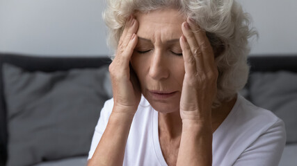 Stressed frustrated elderly woman feeling strong painful headache, holding head, touching and massaging temples with closed eyes. Migraine, dizziness, high blood pressure, healthcare concept, Close up