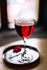 A red alcoholic cocktail in a nick and nora glass served on a tray with cranberry garnish, shot with back light. A lifestyle vertical photo with shallow depth of field.