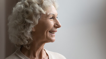 Side view portrait of happy old 70s woman looking away, dreaming and smiling. Pensive senior pensioner lady thinking of good health, retirement, insurance benefits, dreaming of future. Close up