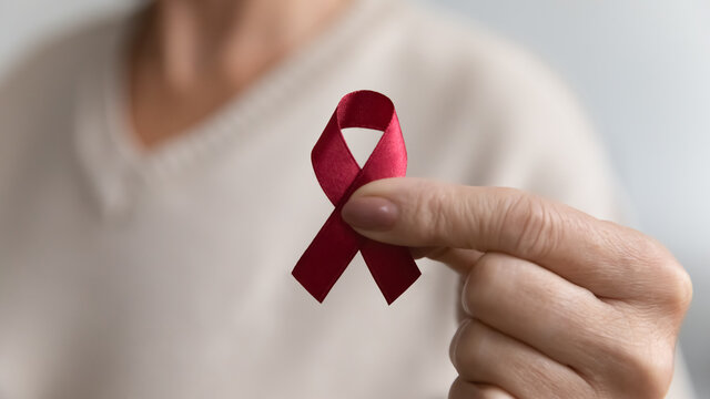 Lady showing hiv or aids awareness symbol, volunteering for charity campaign for prevention immunity disease, cancer, elderly healthcare support. Hand of mature woman holding red ribbon. Close up