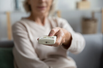 Hand of mature lady operating remote controller, using conditioner for cooling hot air, regulating...