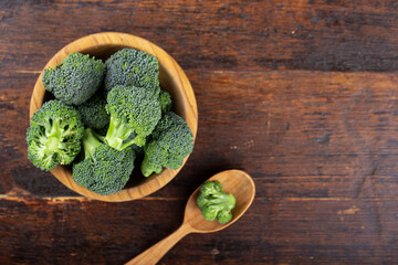 Fresh raw broccoli in a wooden bowl on a wooden table. View from above.