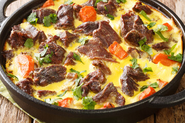 Delicious baked beef with vegetables in egg sour cream sauce close-up in a frying pan on the table. horizontal