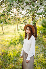 Smiling woman with the hat posing in blooming spring park. The concept of relax, travel, freedom and spring vacation. Fashion style.