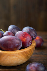 Fototapeta na wymiar Fresh plums in a wooden bowl on a brown table.