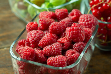 Fresh berries of gooseberries, raspberries and red currants in a glass dish on a wooden table. The concept of healthy food