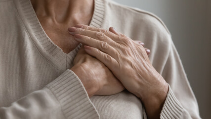 Mature elderly woman feeling heart pain, touching chest with both hands. Thankful senior lady expressing gratitude, love, trust, thanking god, making grateful honor kindness gesture. Close up - Powered by Adobe
