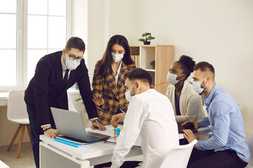 Multiracial team all in face masks working on business project in office meeting. Multiethnic people trying to keep safety measures and take precautions against Covid 19. Coronavirus pandemic concept