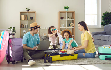 Happy young family packing bags for vacation trip. Parents and kids getting ready for cruise holiday and putting all necessary things and beach clothes to wear in modern travel suitcases together