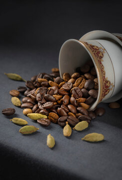 Roasted arabic coffee beans and green cardamom spilling out from a coffee cup. Roasted arabic coffee beans with cardamom.