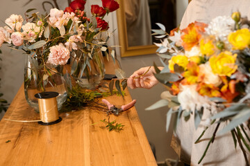 Florist works with colors. Flower seller chooses flowers for future bouquet. Flowers shop worker in a mask standing in flower shop and checking flowers in glass vase.