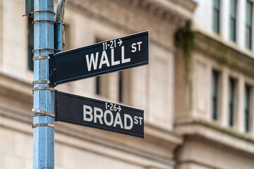 Wall Street "WALL ST" sign and broadway street over American national flags in front of NYSE stock market exchange building background. The New York Stock Exchange locate in economy district
