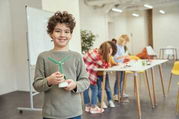 Little engineer. Portrait of adorable boy showing mechanical toy he assembled by himself on crafting classes while posing for camera during STEM lesson