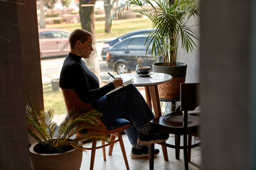 Young girl with short hair and nose piercing sits in a cafe and work at a tablet. The concept of freelancing and remote work.