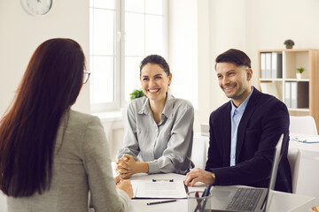 Young happy family couple meeting with bank worker to sign loan contract discussing banking credit, personal insurance or mortgage investment. Focus on cheerful smiling clients face sitting at table