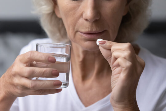 Mature Senior Lady Taking Pills For Relieving Mental Disease, Memory Loss, Dementia Symptom, Holding Aspirin Or Painkiller Med And Glass Of Water. Close Up Of Hands With Medication An Lower Face.