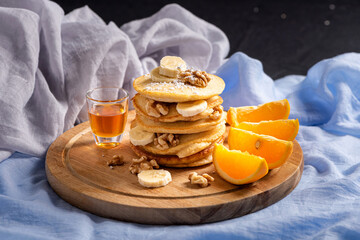 Stack of pancakes with honey, nuts, bananas and oranges