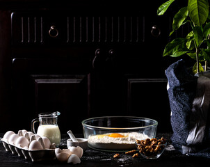 Scene with ingredients for baking such as flour, eggs and milk against a dark rustic background