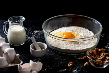 Scene with ingredients for baking such as flour, eggs and milk against a dark rustic background
