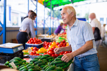 Fototapeta na wymiar retired european man buys cucumbers and tomatoes in market
