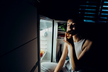 Portrait of a beautiful girl taking food from the refrigerator at night. Night food, overeating concept. Diet, dieting. Beauty young woman eating dessert in refrigerator in night kitchen.