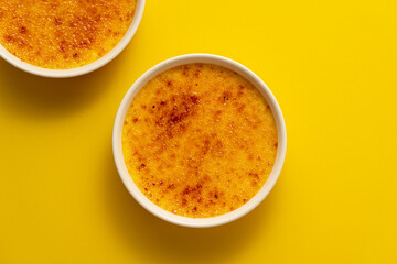 Creme brulee in two ramekin isolated on bright yellow color background. Close up french dessert. Burned cream. Spanish crema catalana. Top view