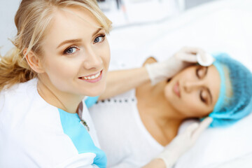 Fototapeta premium Professional beautician and young woman in beauty salon. Makeup artist touch customer skin with cotton pads, closeup. Cosmetology , facial, beauty and spa