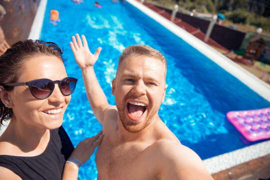 Couple of friends make selfie photo, happy caucasian beautiful young woman and man hug traveling on background hotel pool