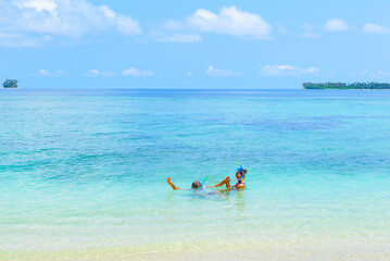 Fototapeta na wymiar Happy adult couple having fun in turquoise water wearing snorkeling mask. Real people bathing in caribbean sea on tropical beach, islands in the background