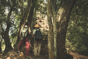 Couple looking at stone faces in the jungle, Bayon Temple Angkor Thom. Buddhism meditation concept, world famous travel destination, Cambodia tourism.