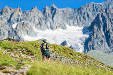 Fototapeta na wymiar Woman with backpack hiking towards mountain top, scenic glacier and dramatic landscape summer fitness wellbeing selective focus rear view, freedom concept