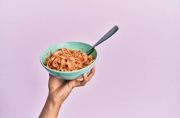 Hand of hispanic man holding bowl with italian noodles over isolated pink background.