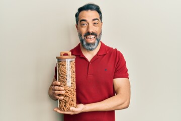 Fototapeta premium Middle age man with beard and grey hair holding jar with macaroni pasta celebrating crazy and amazed for success with open eyes screaming excited.