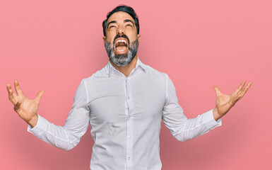 Middle aged man with beard wearing casual white shirt crazy and mad shouting and yelling with aggressive expression and arms raised. frustration concept.