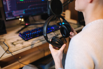 Closeup of man wearing headphones during the work with music at home. Background of micrphone and pc with keyboard. Neon light