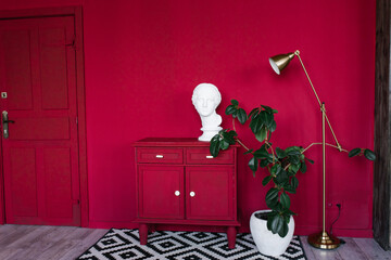 Stylish interior of the room with scarlet walls, a red chest of drawers, a female head sculpture, a...